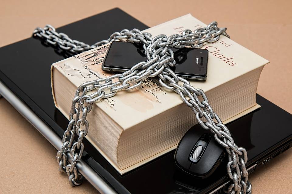 a steel chain wrapped around a laptop with a mouse, a phone, and a book to display security